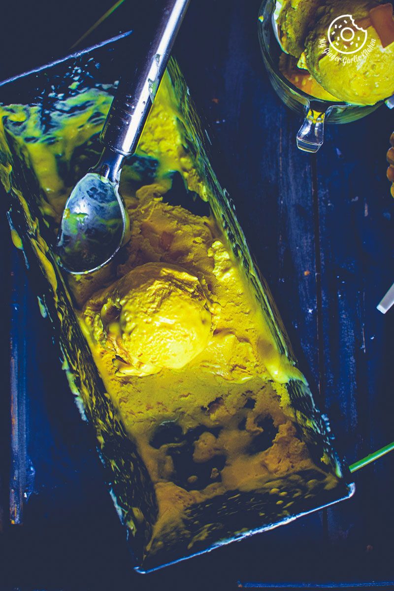 a yellow mango ice cream in a metal container with a spoon