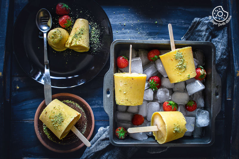 two plates of mango kulfi, with ice cubes and strawberries on a tray