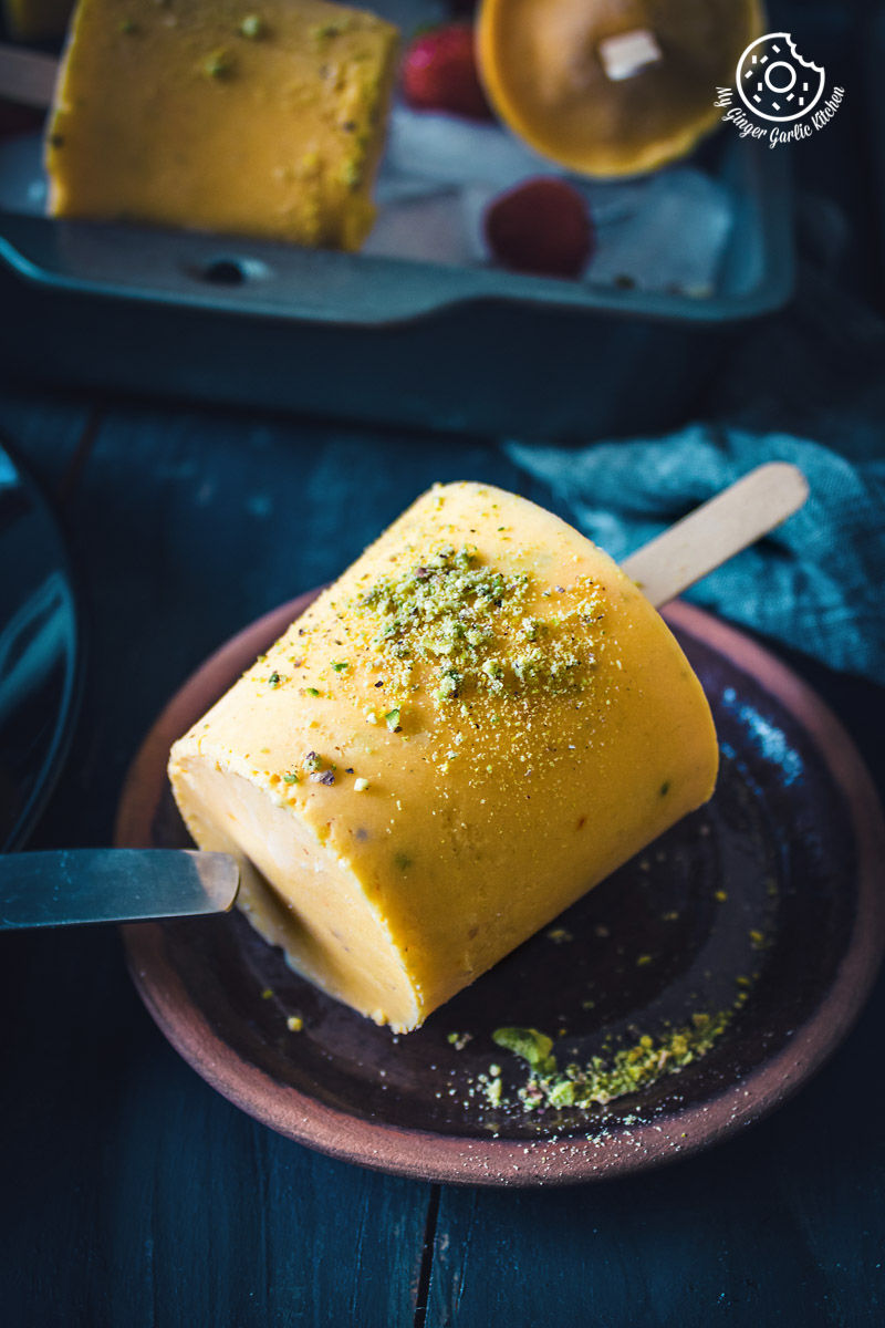 a piece of mango kulfi popsicle on a plate topped with ground pistachios