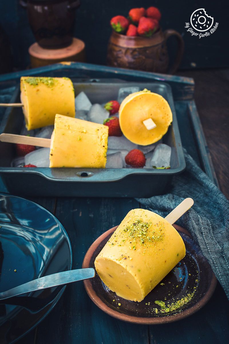four mango kulfis on a plate with strawberries and a spoon