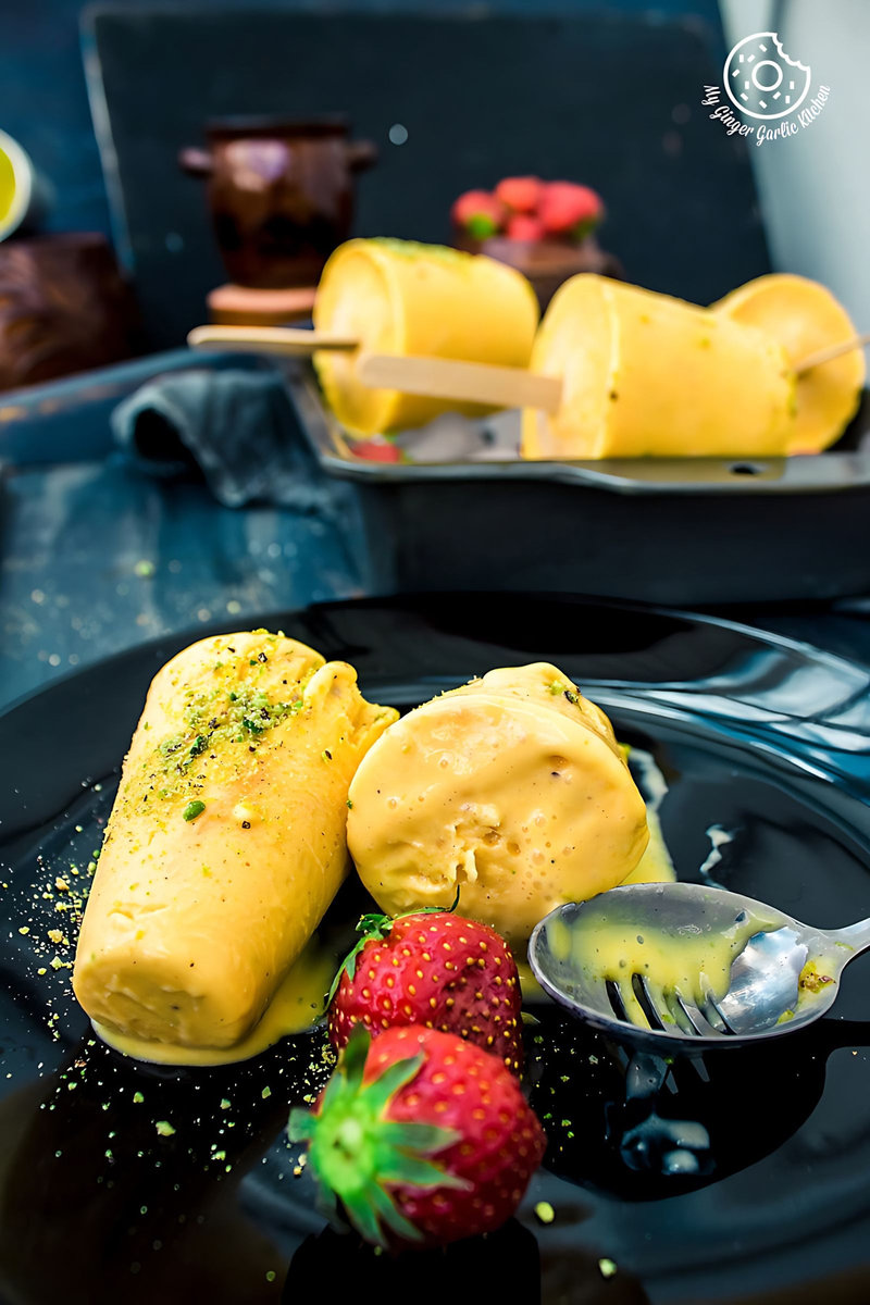 two mango kulfis on a plate with a spoon and a spoon