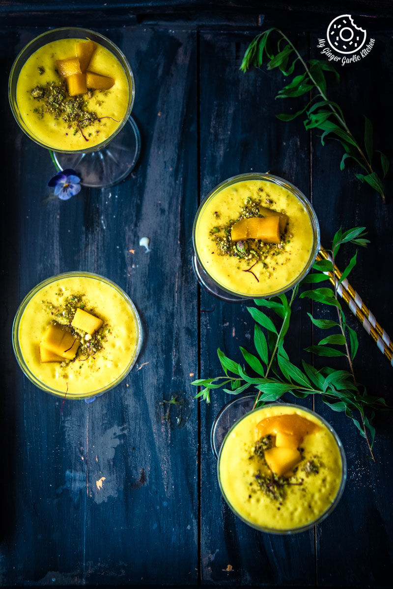 several glasses of mango lassi sitting on a table with a straw