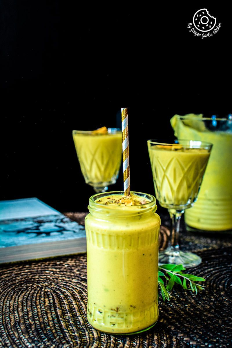 a glass of a mango lassi with a straw and few more glasses