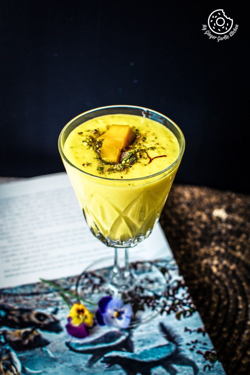 a mango lassi drink topped with pistachios in a glass on a table
