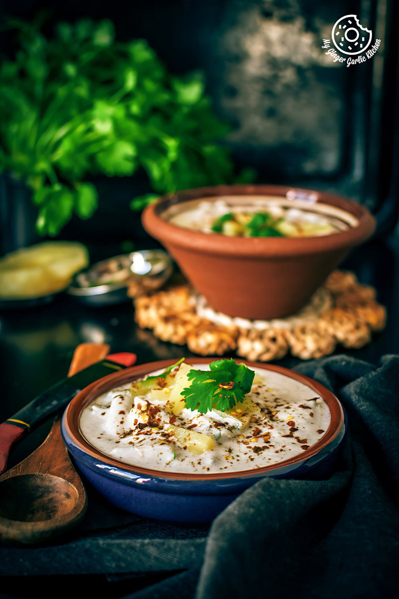 a bowl of pineapple raita topped with cilantro and a spoon on the side