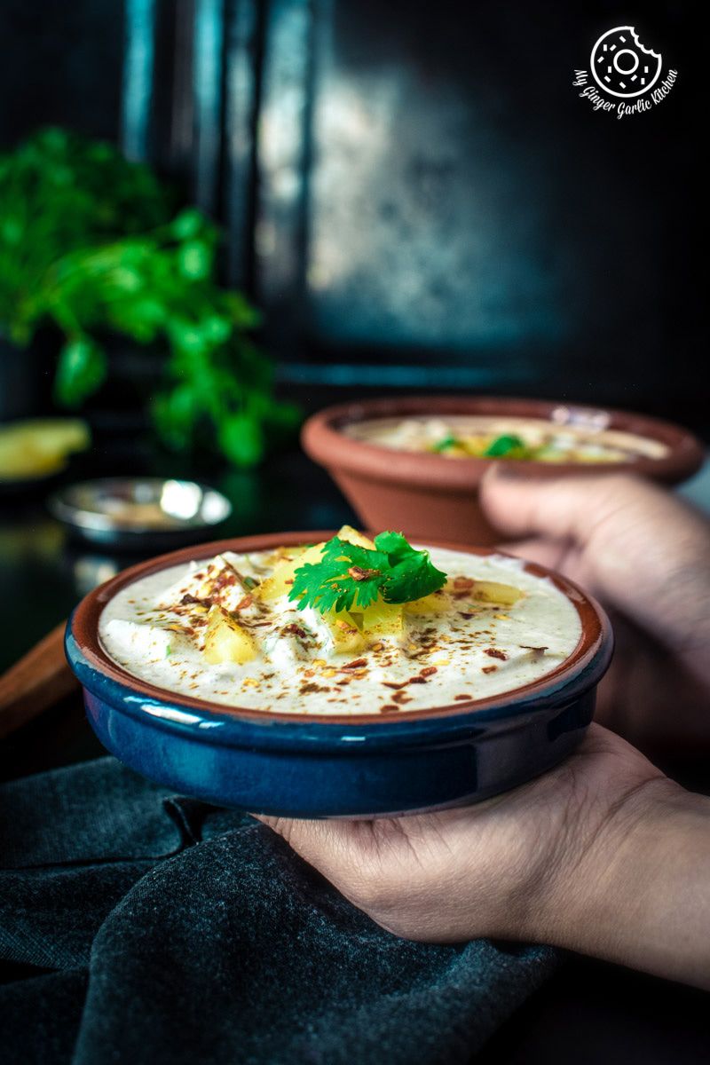 someone holding a bowl of pineapple raita with a green garnish on top