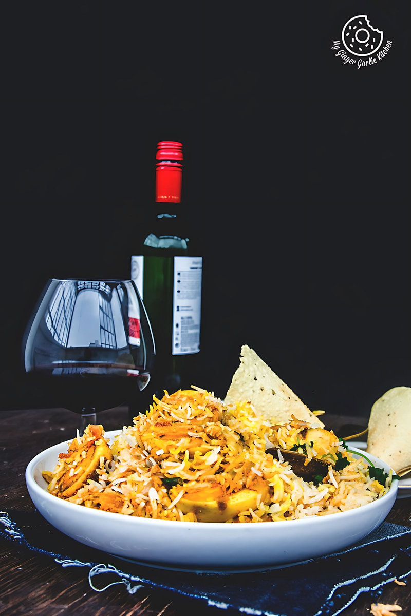 a plate of hyderabadi egg biryani with a glass and a bottle of wine