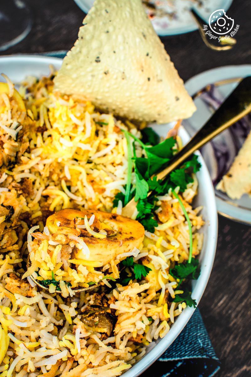a plate of hyderabadi egg biryani with papad and on a table