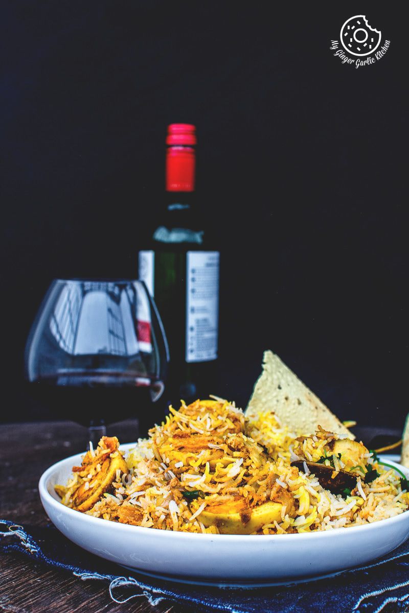a plate of hyderabadi egg biryani with a glass of wine in the background