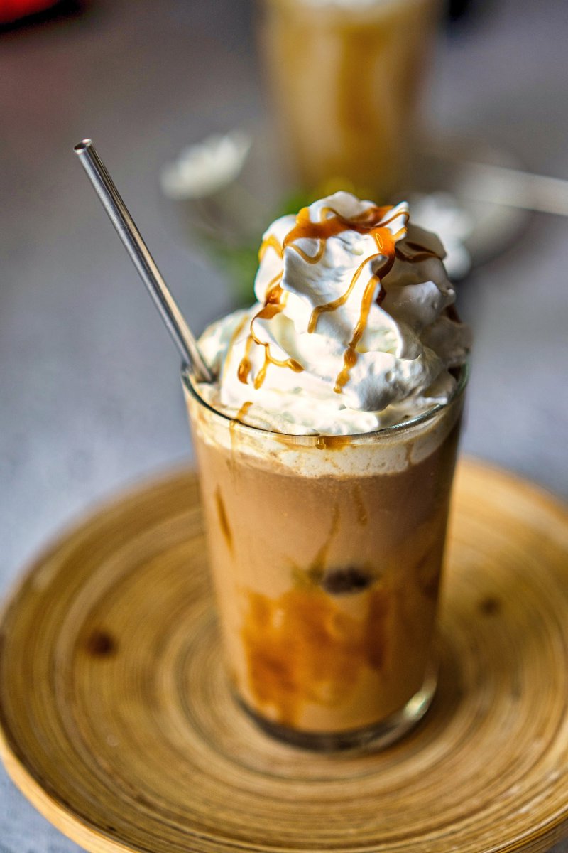 Close-up of an iced caramel latte topped with whipped cream and caramel drizzle, served with a metal straw.