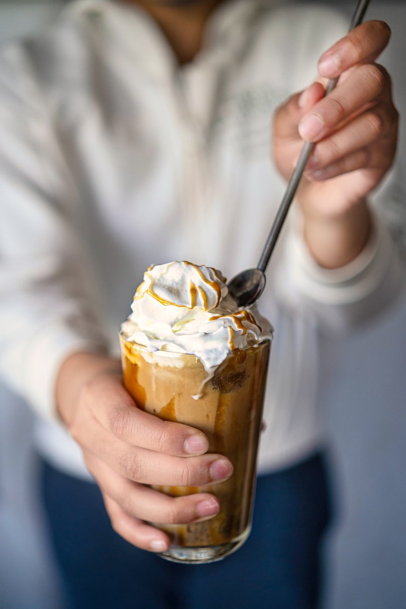 Person holding a glass of iced caramel latte topped with whipped cream and caramel, ready to be enjoyed.
