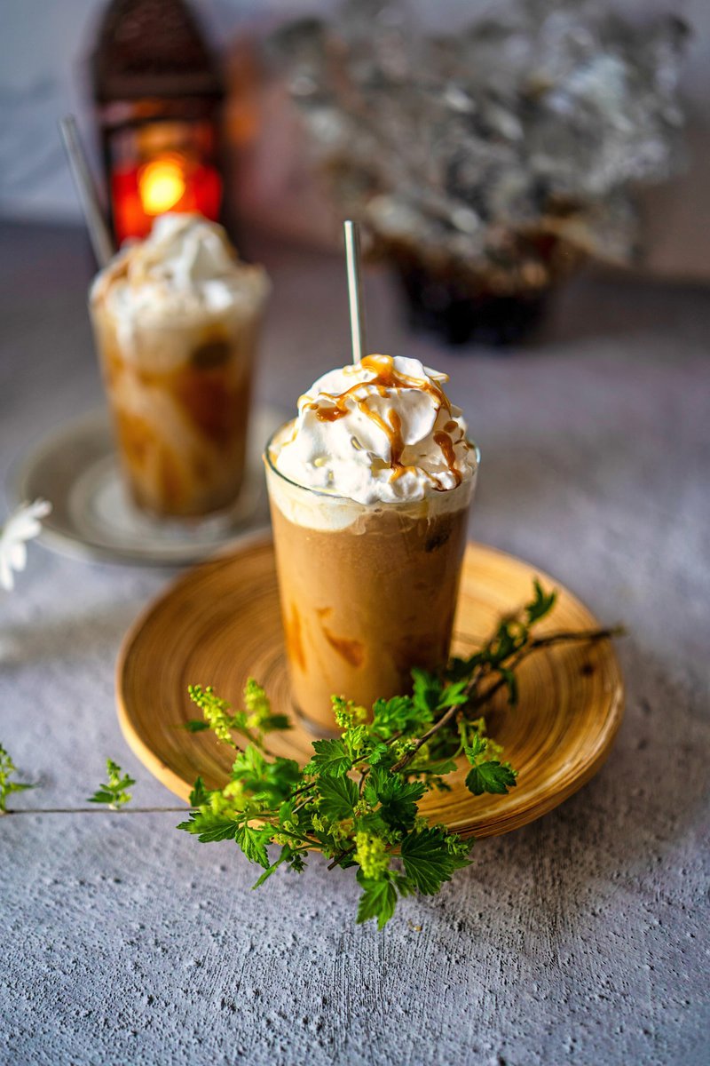 Elegant presentation of two iced caramel lattes on a wooden plate, garnished with fresh herbs, in a cozy setting.