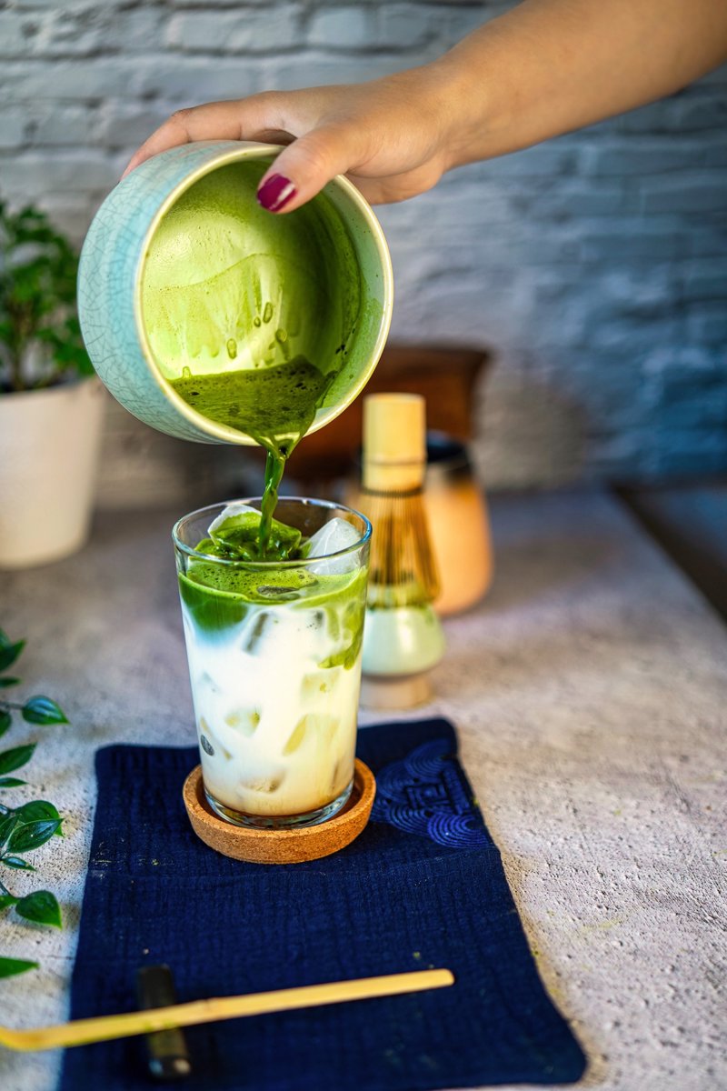Homemade iced matcha latte being poured over ice and milk from a matcha bowl