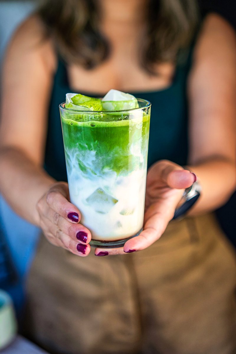 Fresh iced matcha latte held in hands showing creamy milk, vibrant green matcha, and ice
