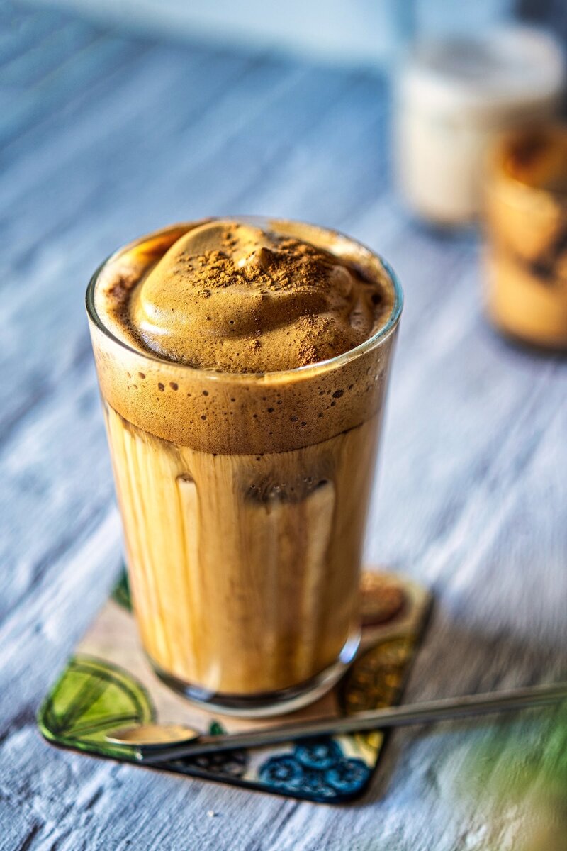 Creamy iced oat milk dalgona latte topped with thick frothy coffee foam and cinnamon in a glass