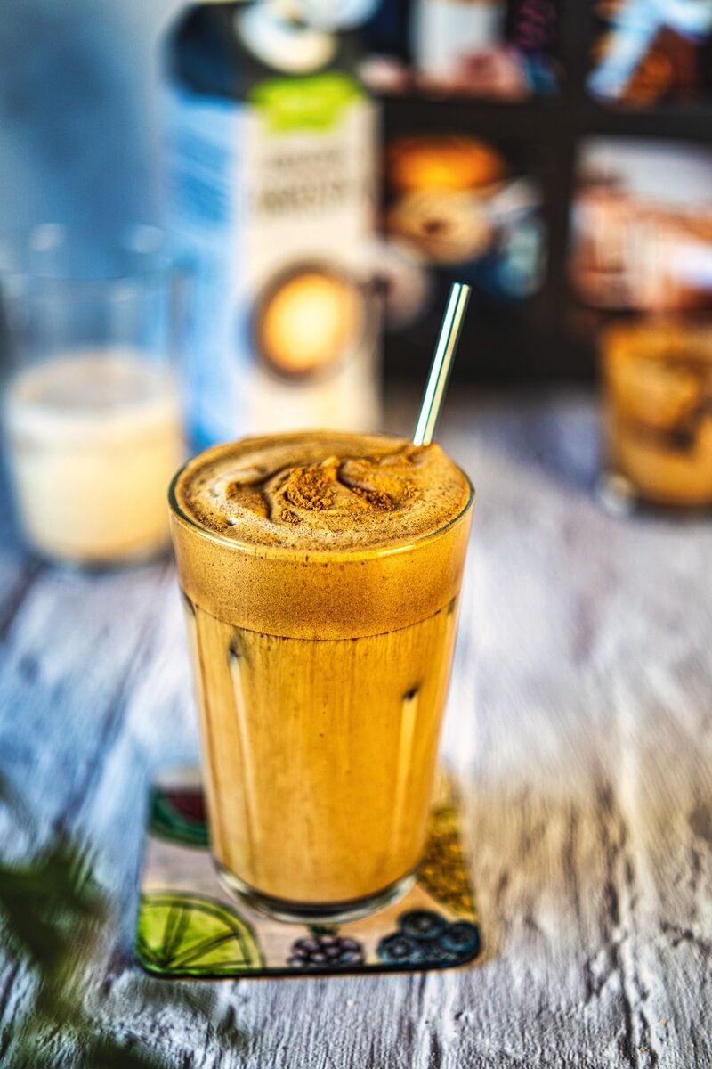 Layered iced oat latte with whipped coffee foam and straw, vegan dalgona coffee drink in tall glass