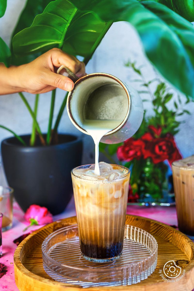 Image of the iced rose latte. A hand is pouring milk into the glass.