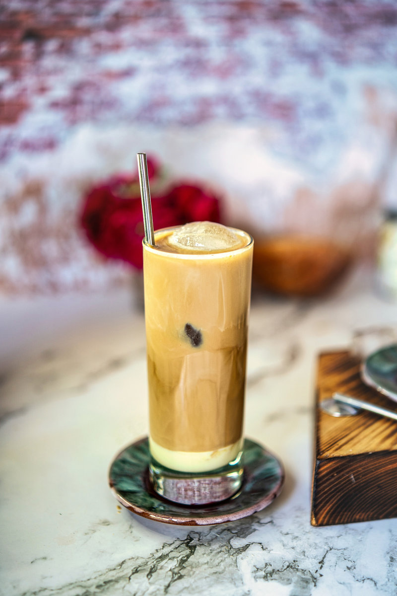 A refreshing Iced Spanish Latte with a metal straw, filled with ice cubes, perfect for a warm day.