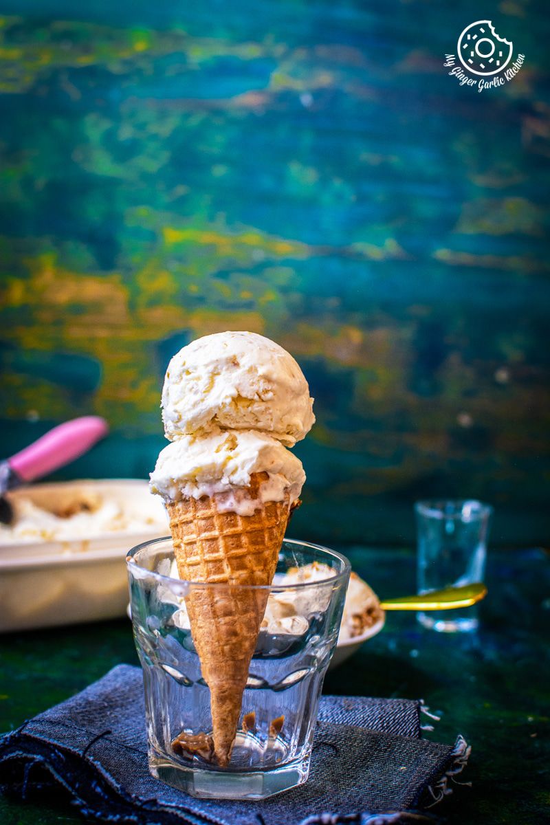 an ice cream cone with two scoops of butterscotch ice cream in a glass cup on a napkin