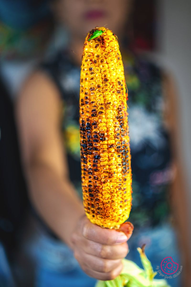 a closeup shot of someone holding indian roasted corn on the cob - masala bhutta