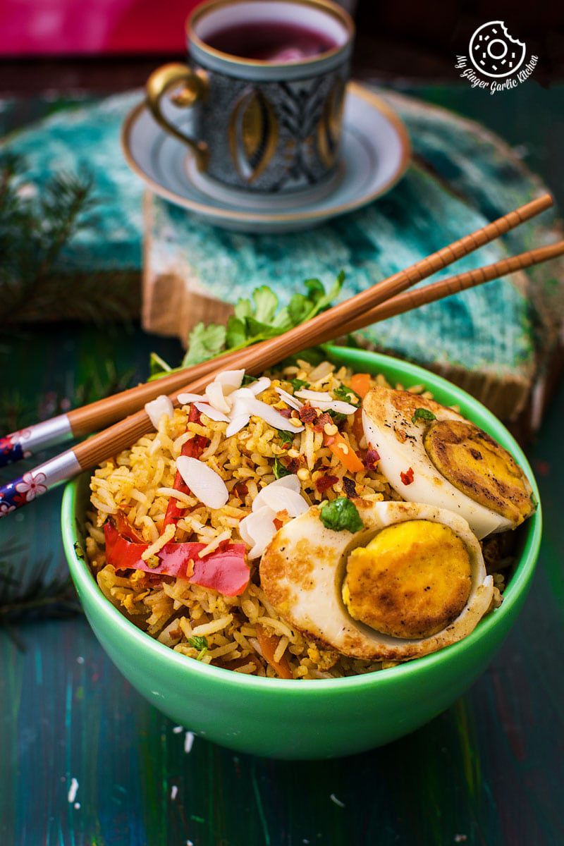 a bowl of indian style triple egg fried rice with chopsticks and a cup of tea