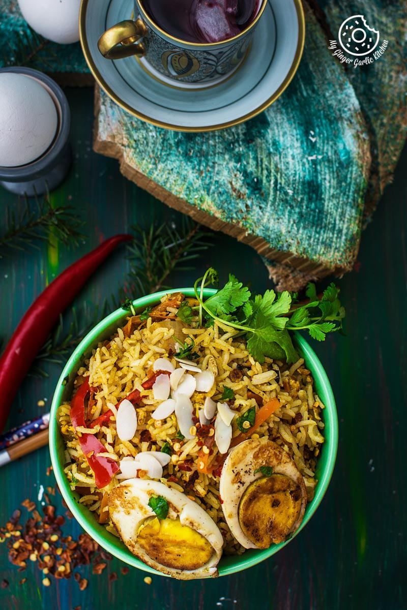 a bowl of indian style triple egg fried rice with almond flakes, chopsticks and a cup of tea