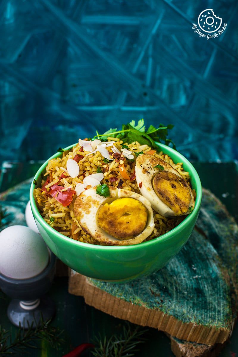 a bowl of indian style triple egg fried rice with almond flakes, and eggs on a table