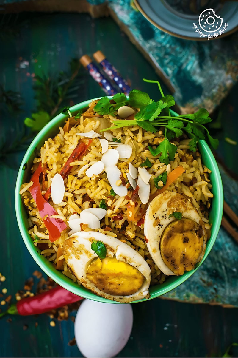 a bowl of indian style triple egg fried rice with almond flakes, chili, and egg on a table