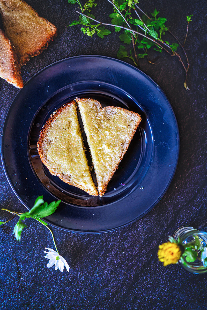 Top view of Indian sweet bread slices on a black plate divided into triangles with herbs and a small flower on the side.
