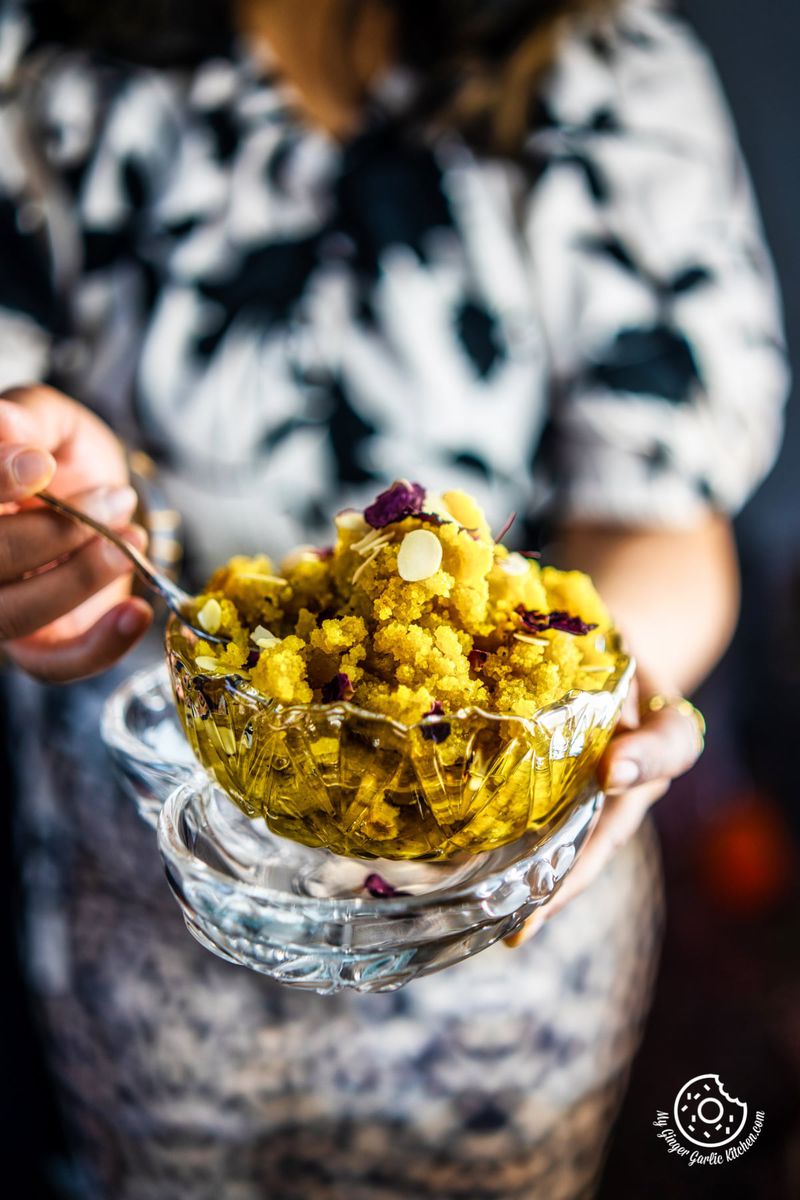 a female holding a transparent bowl of instant badam halwa