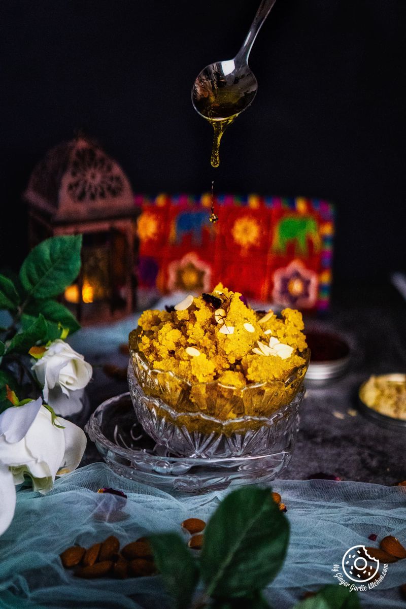 ghee is drizzling from a spoon over instant badam halwa bowl