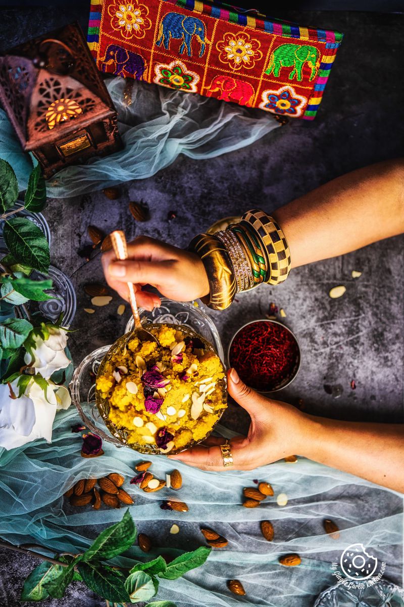 overhead shot of female hands holding instant badam halwa served in a transparent bowl