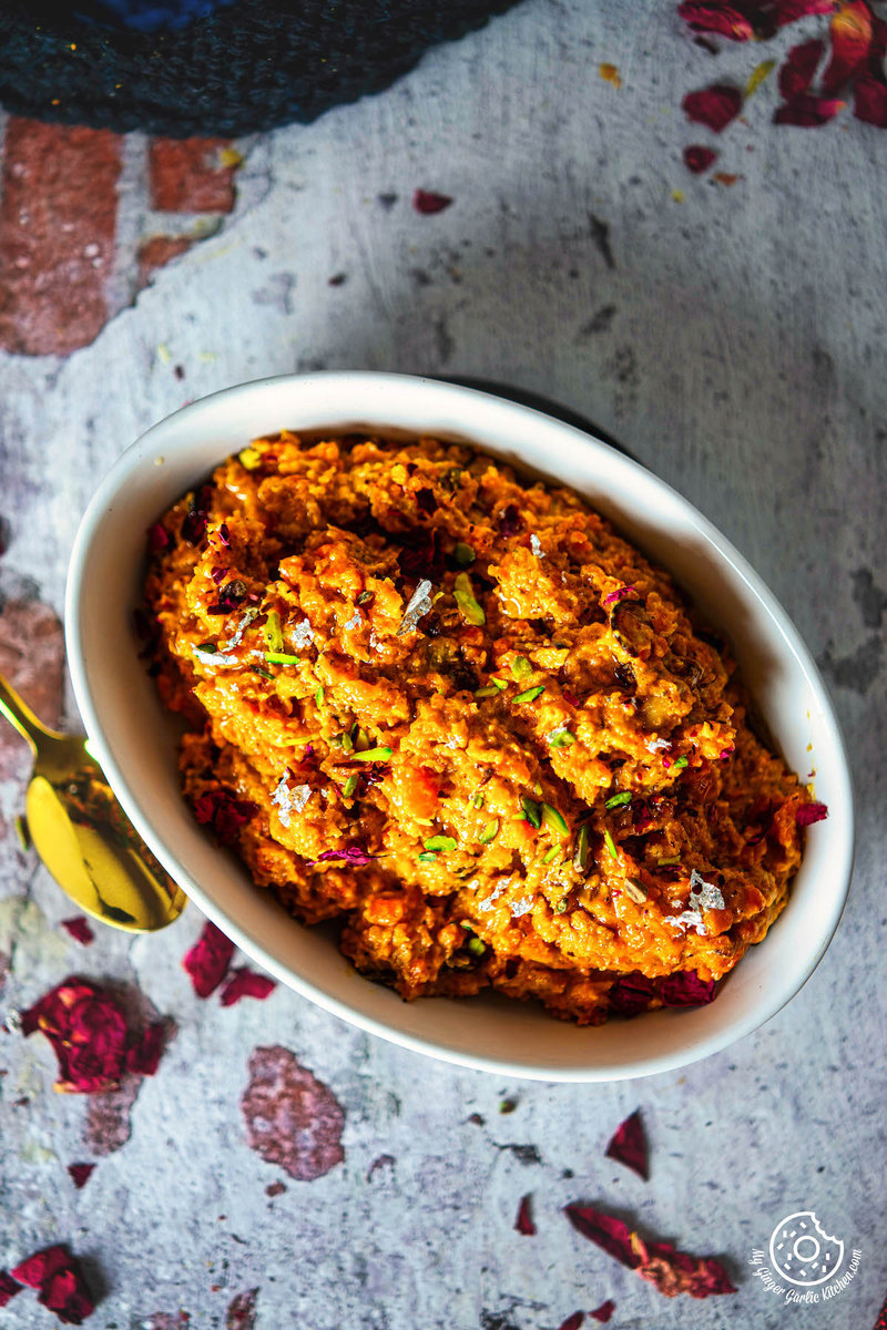 a bowl of pressure cooker gajar halwa ganrished with dried rose petals on a table