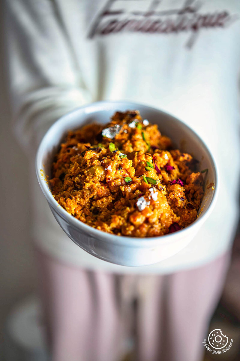someone holding a bowl of instant gajar halwa with a lot of food in it