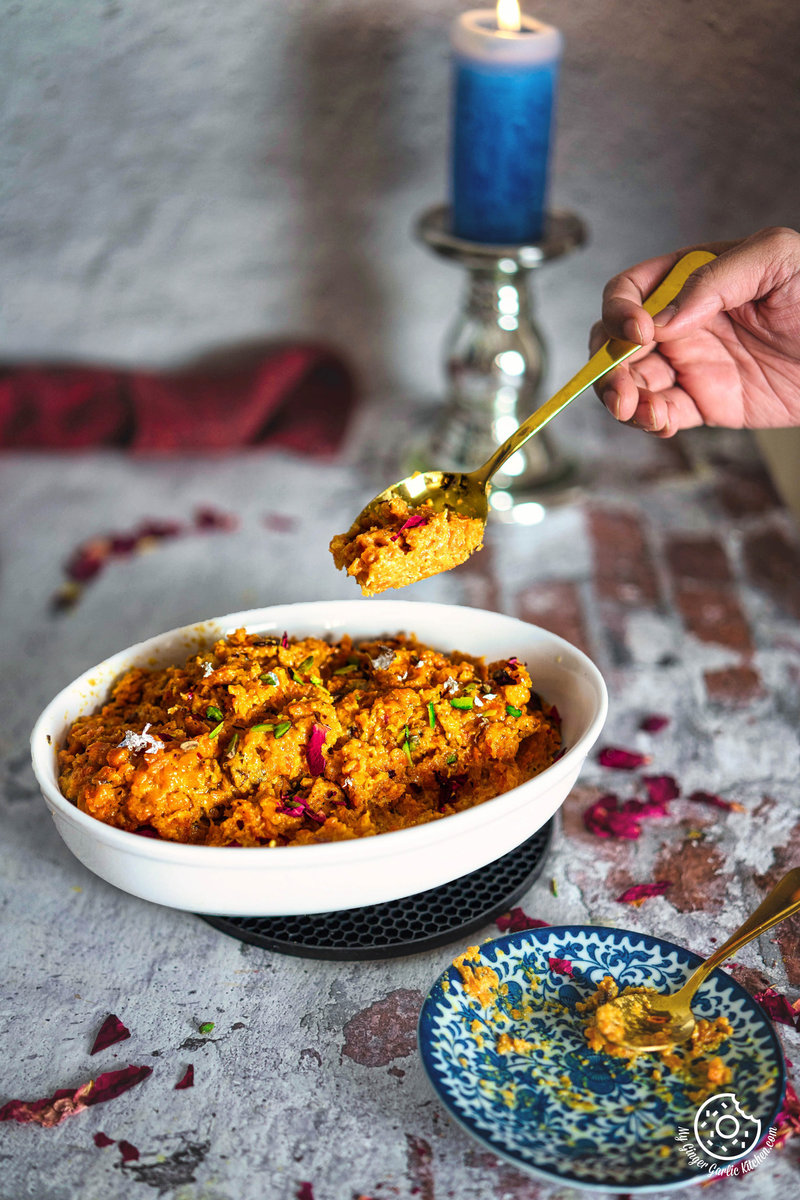 someone is holding a spoon over a bowl of instant gajar ka halwa with a candle in the background