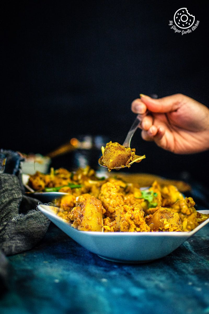 a hand holding a spoon filled with aloo gobi