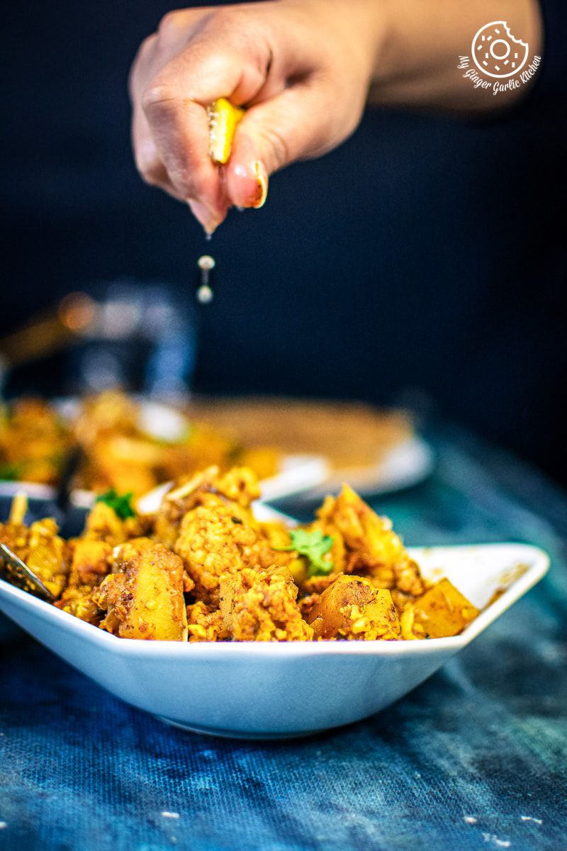 a hand is squeezing lemon over instant pot aloo gobi bowl