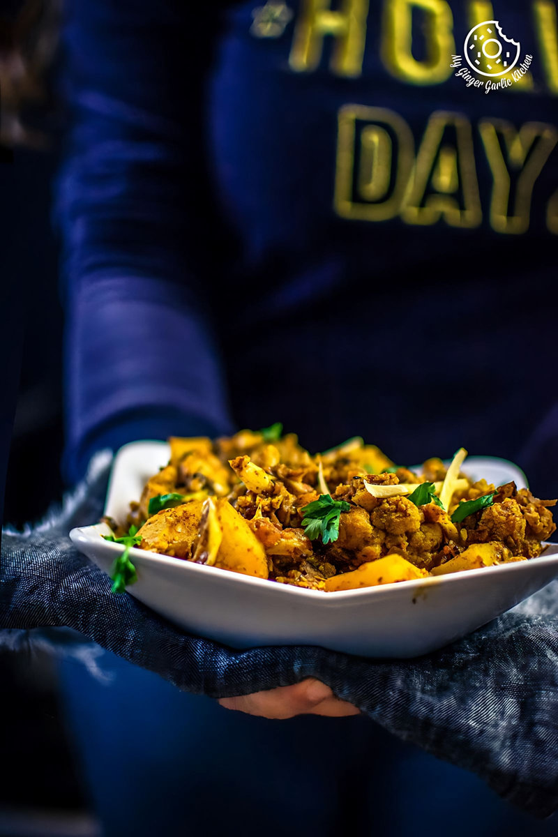 a person holding a bowl of aloo gobi