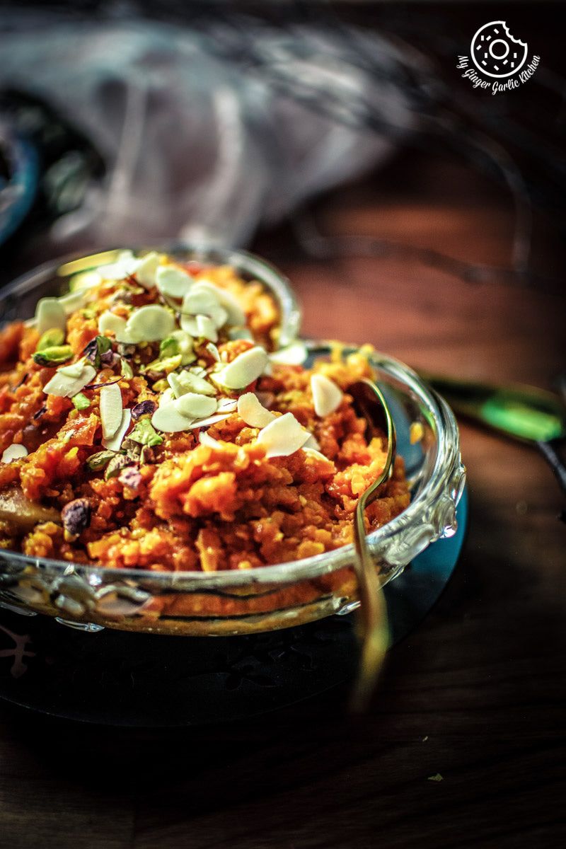 a bowl of instant pot gajar halwa topped with nuts and a spoon on the table