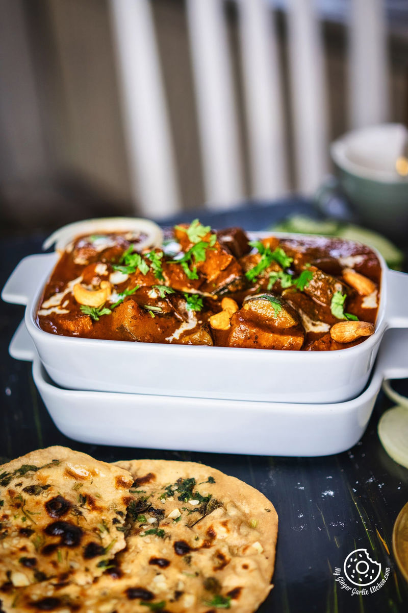 zucchini tofu curry topped with cilantro and cream served in a white rectangular casserole dish and some naan on the side