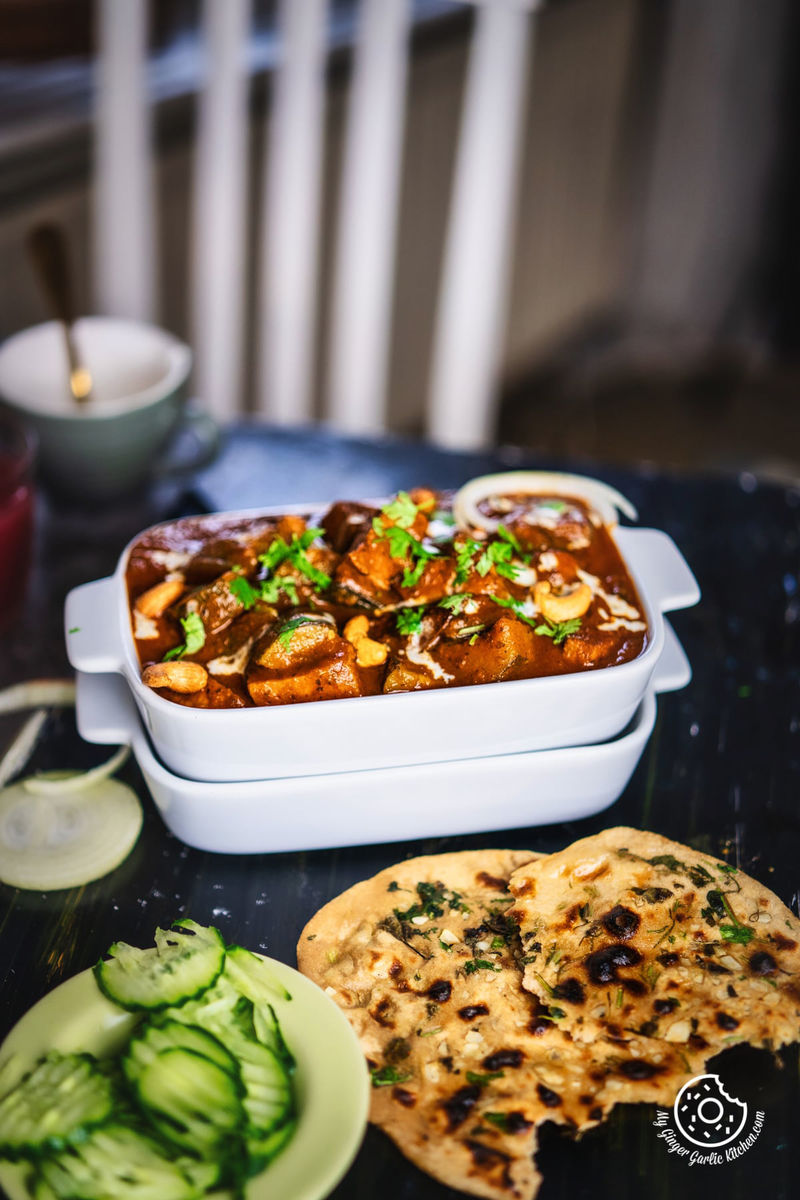 zucchini tofu curry topped with cilantro and cream served in a white rectangular casserole dish and some naan and cucumber slices on the side