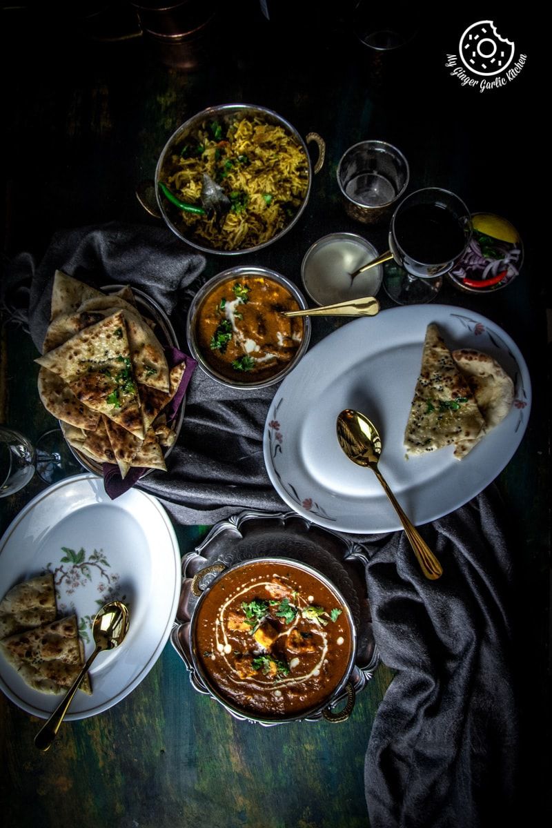 several plates of instant pot butter paneer with biryani and naan on a table with a cloth