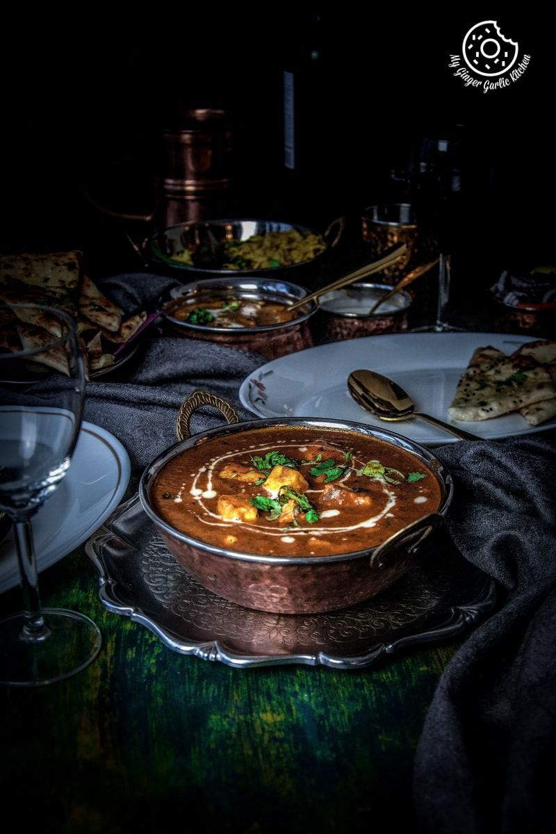 a bowl of instant pot butter paneer on a table with plates of naan and other indian food