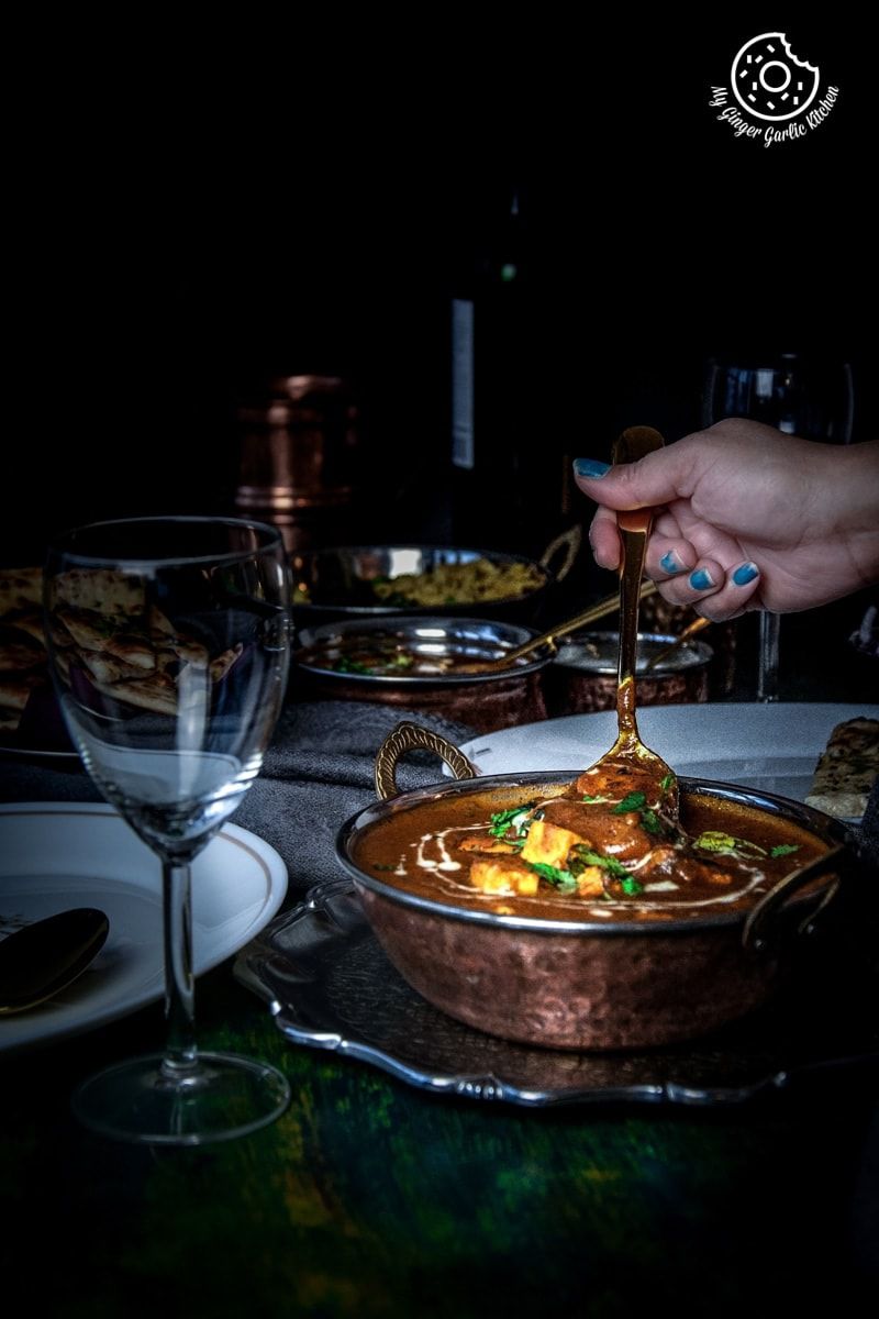 someone is serving a bowl of instant pot butter paneer on a table with a glass of wine