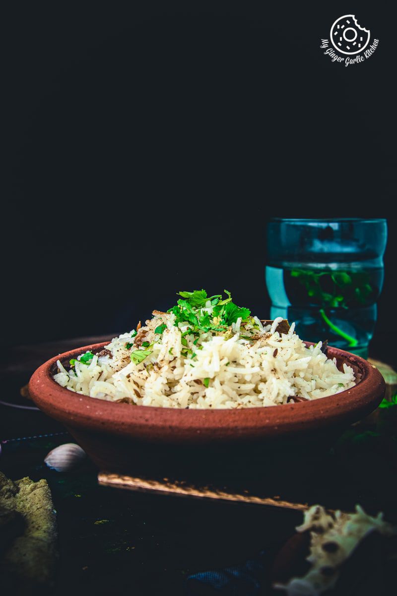 a brown bowl of cumin rice is sprinkled with some cumin powder and coriander leaves