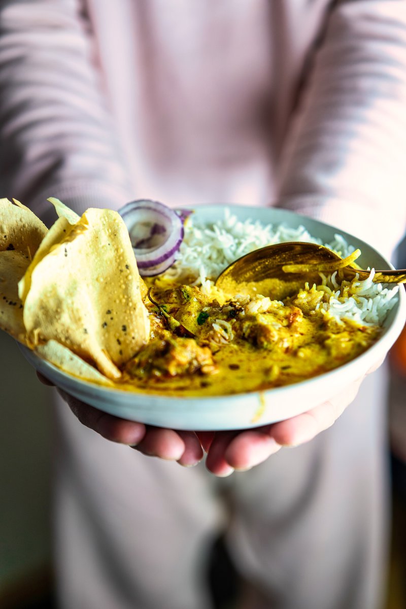 Person holding a bowl of Kadhi Pakora with rice, showcasing a traditional Indian meal in a casual setting.