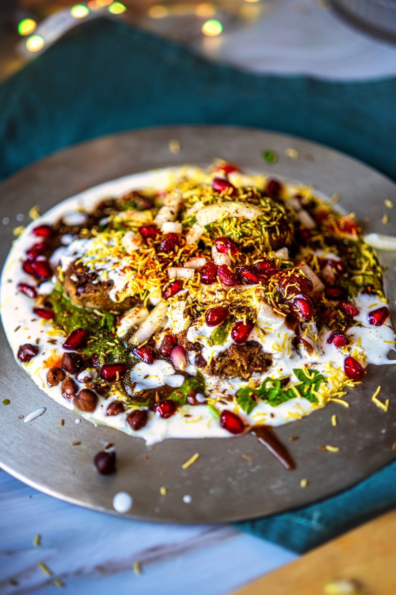 A vibrant Kala Chana Tikki Chaat served on a plate, garnished with yogurt, sev, pomegranate seeds, and mint chutney.