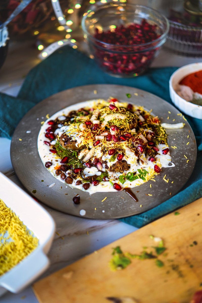 Kala Chana Tikki Chaat garnished with yogurt, pomegranate seeds, sev, and spices on a plate.