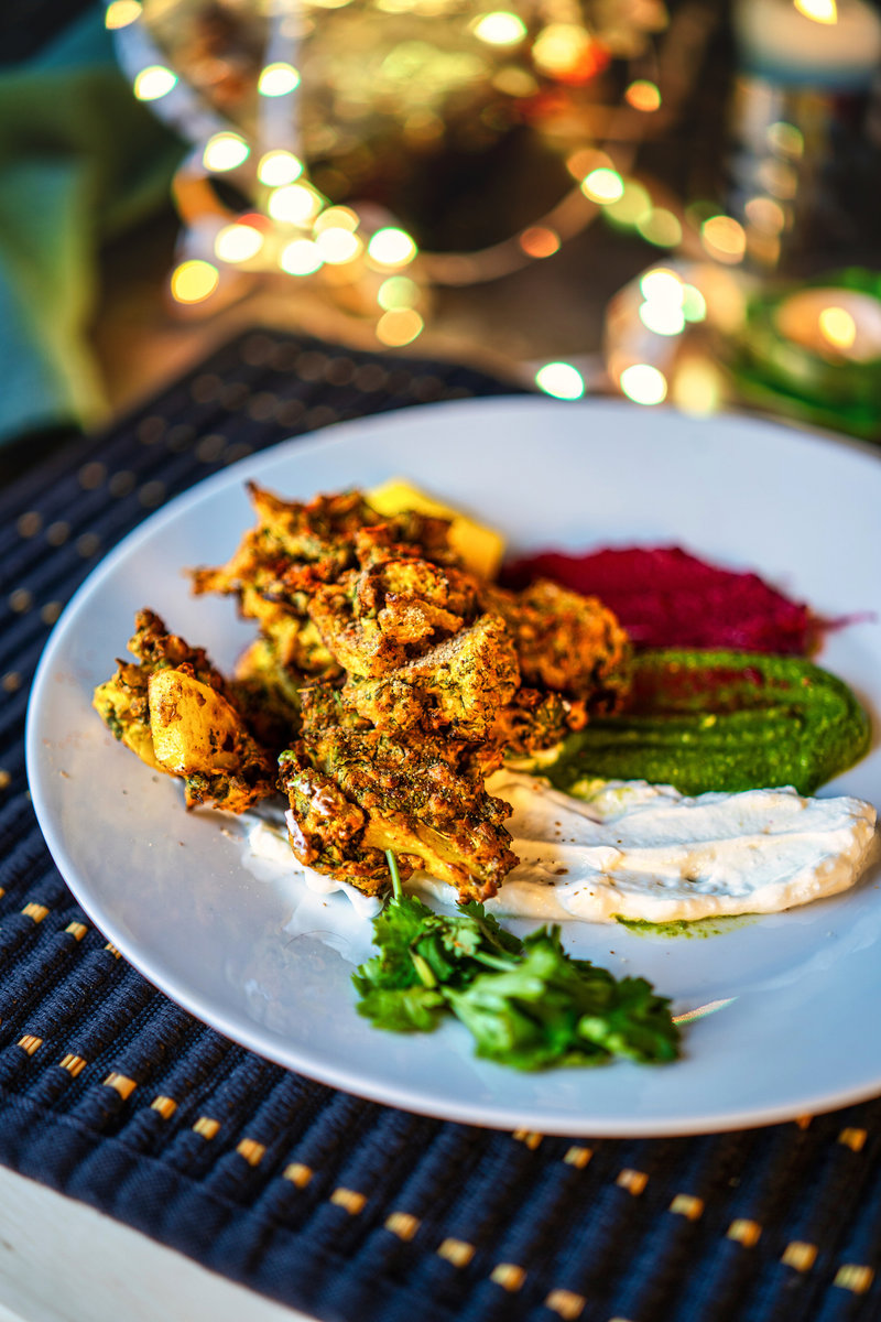 A plate of crispy kale pakoras served with green, red, and white dipping sauces, garnished with cilantro.