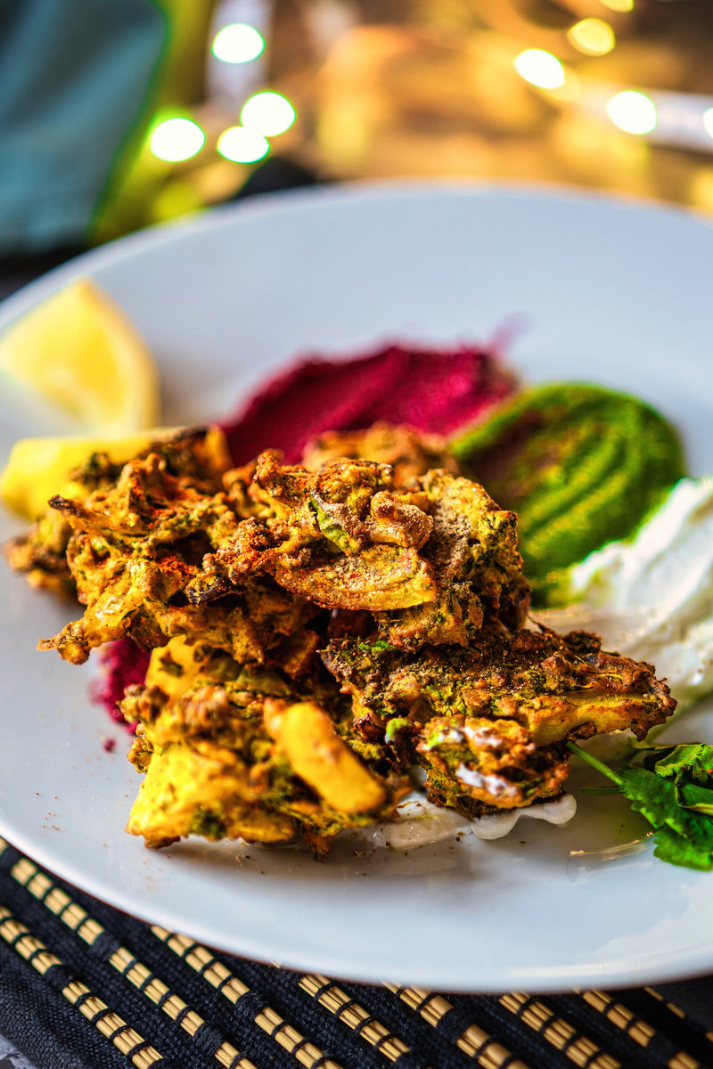 Plate of crispy kale pakoras served with colorful dips and a lemon wedge.